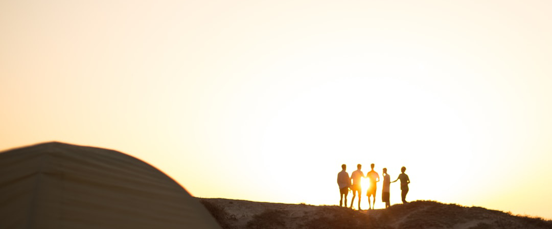 Petit groupe de personnes au sommet d'une coline au coucher du soleil.