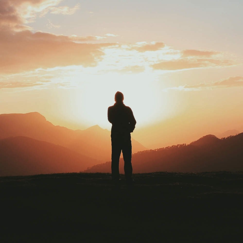 Silhouette d'homme devant le soleil et les montagnes