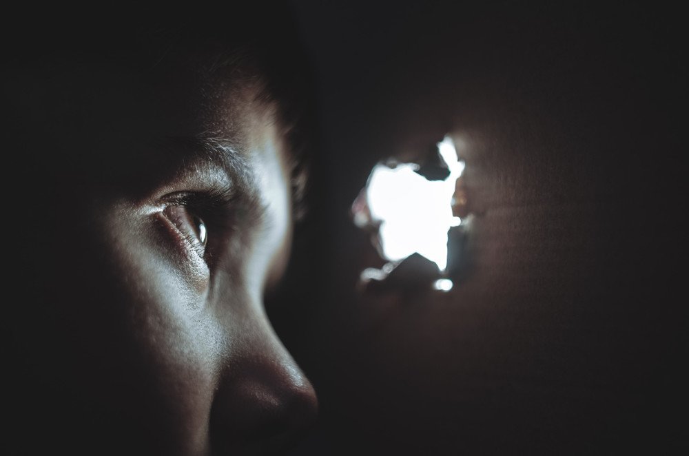 Enfant qui regarde la lumière par un trou dans le mur.