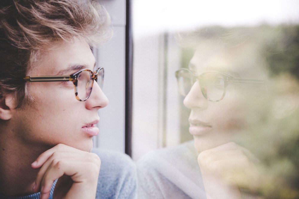 Jeune homme qui regarde son reflet dans une vitre.